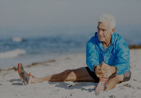 Älterer Herr sitzt im Sand am Strand und dehnt sich